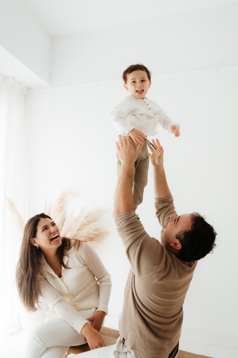 PAPA LANZANDO A SU HIJO HACIA EL AIRE MIENTRAS LA MAMA LOS MIRA FELIZ
